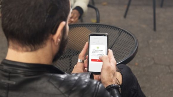 A cochlear implant user sits outside at a café and uses the HearCare MED-EL app to conveniently download a new audio processor configuration from their clinician.