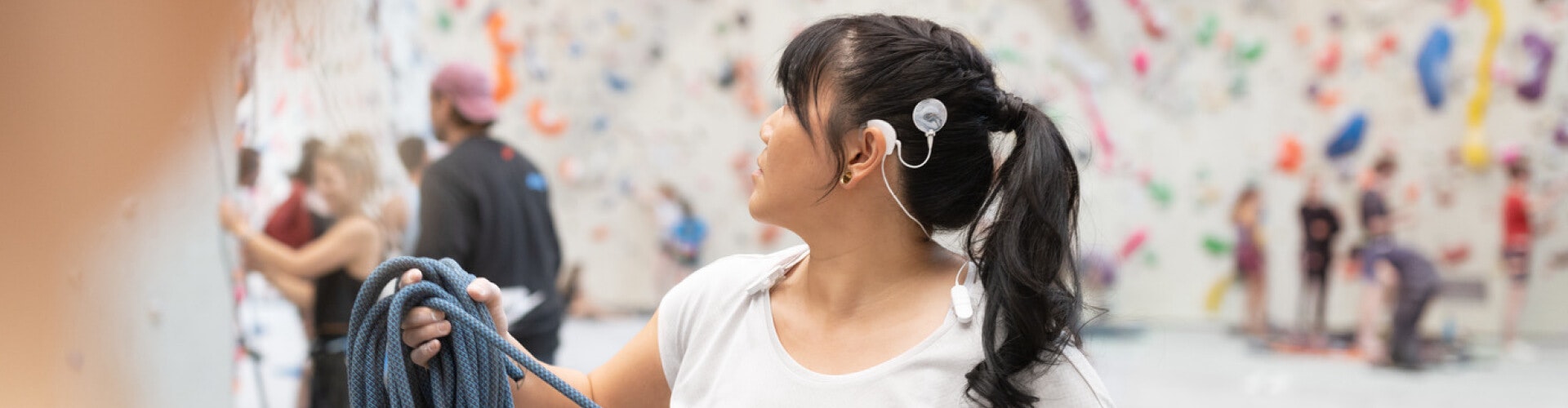 A young woman uses SONNET ActiveWear to secure her SONNET 3 audio processor to her shirt while enjoying indoor climbing.