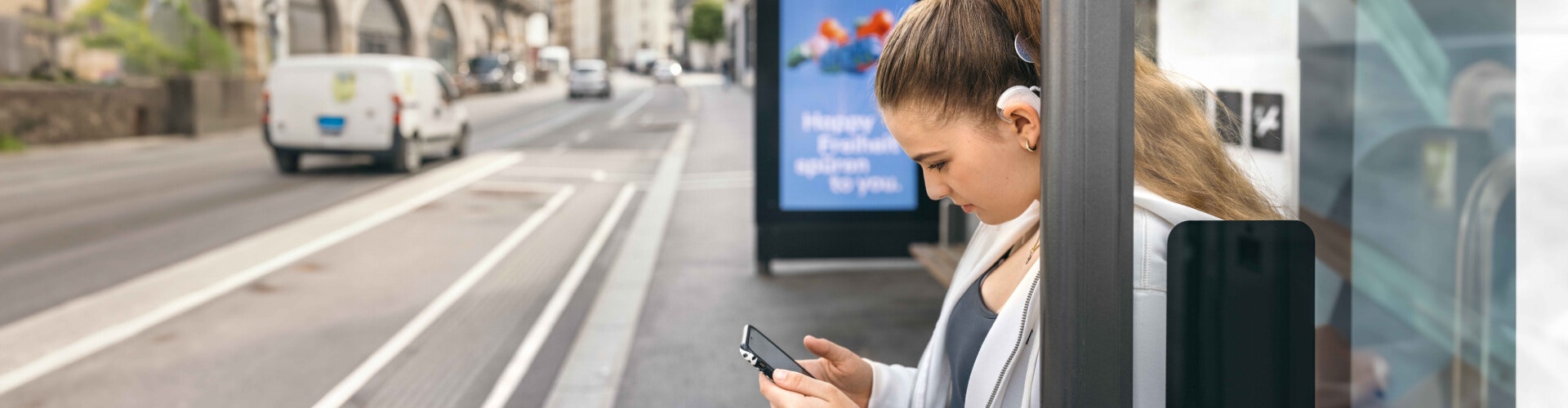 A teenager uses her SONNET 3s to stream music to her ears while waiting for a bus.