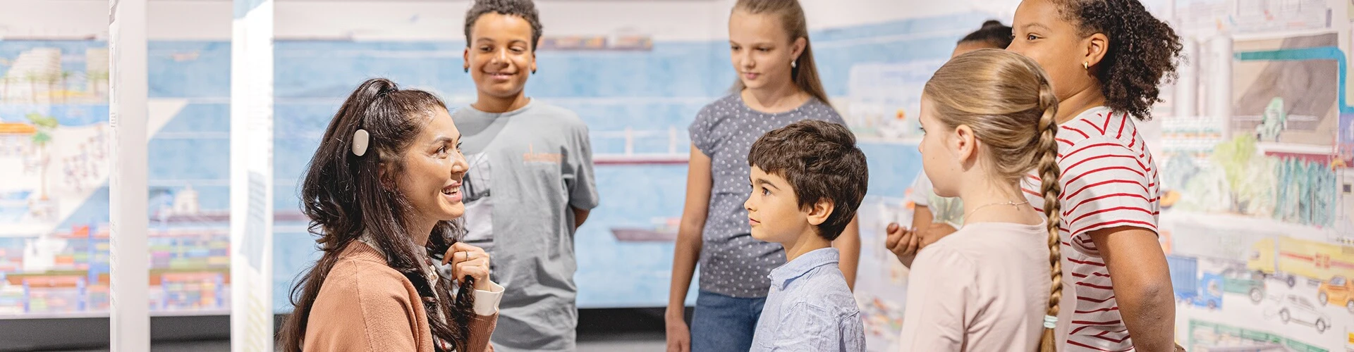 Cochlear implant user working with a group of children, one of whom is also a cochlear implant user.