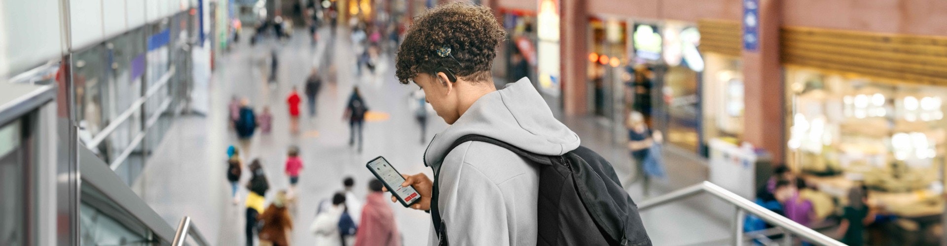 Teenager at a busy train station adjusting SONNET 3 settings with the AudioKey 3 app