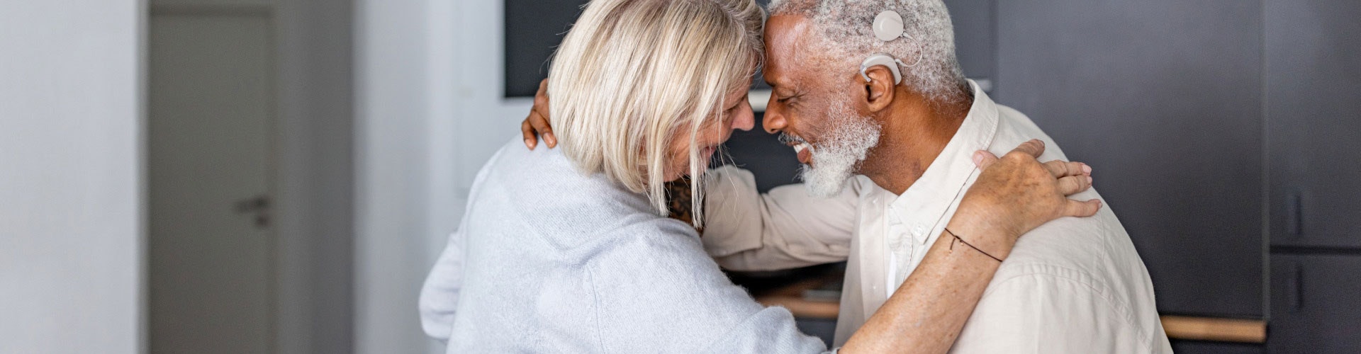 Older couple smiles and dances around the kitchen – one is a cochlear implant user.