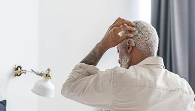 An older man puts on his SONNET 3 cochlear implant audio processor while indoors near a lamp