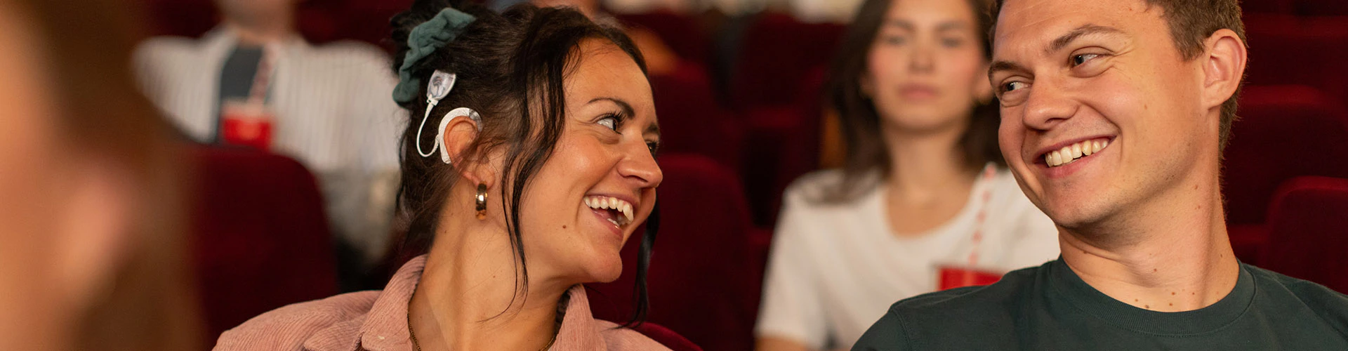 People seated in a theater, with one woman wearing a cochlear implant processor