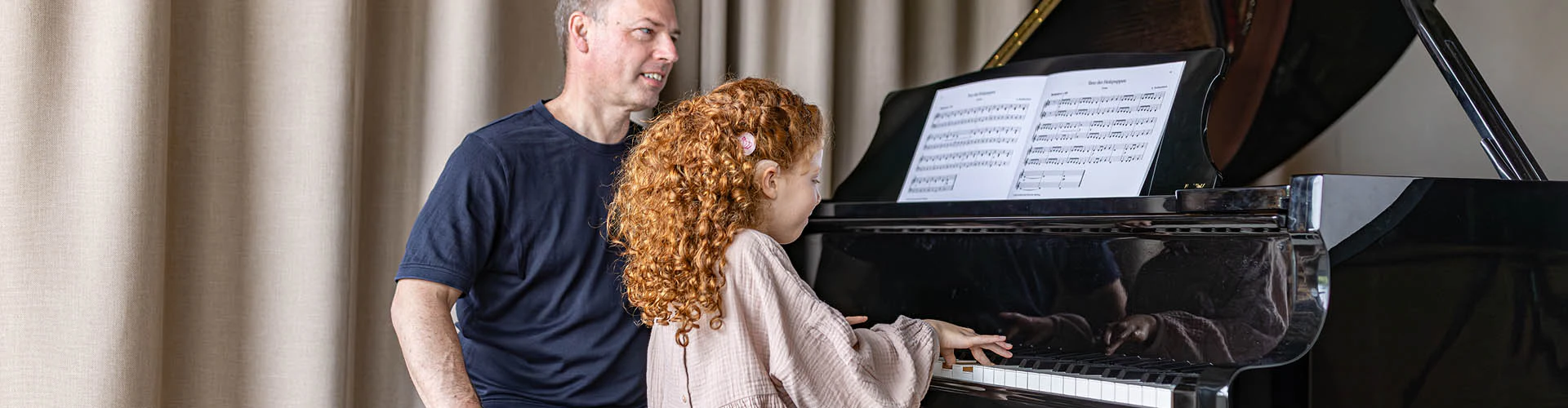Man guiding a girl playing the piano. The child has a cochlear implant audio processor