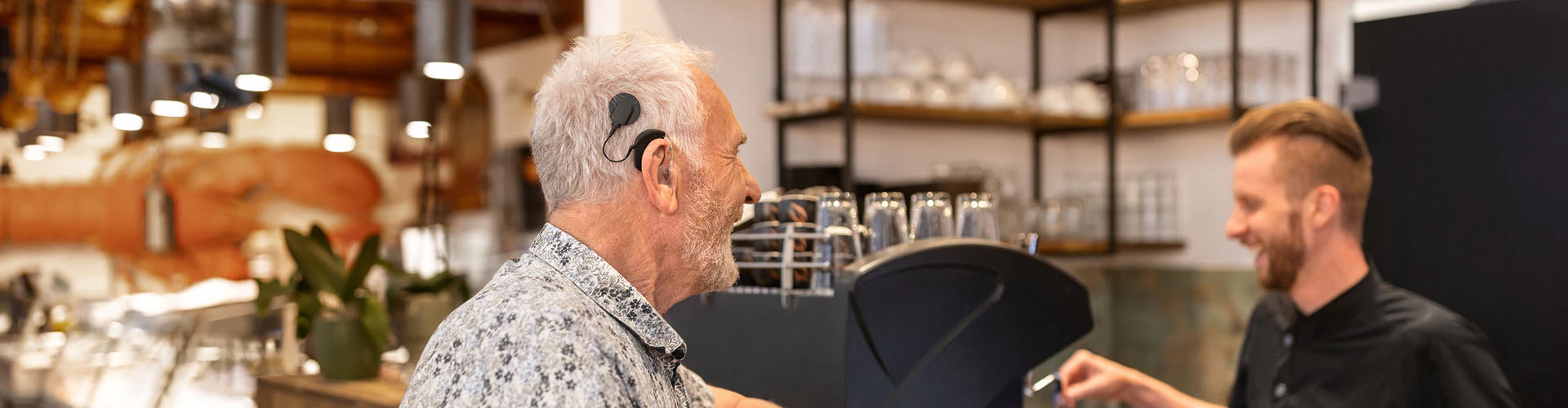 Man with a cochlear implant audio processor ordering a drink at a café counter