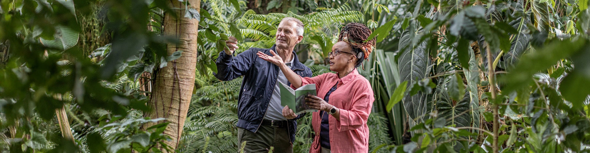 Two people walking through botanical gardens. The woman wears glasses and has a RONDO 3 audio processor behind her ear.