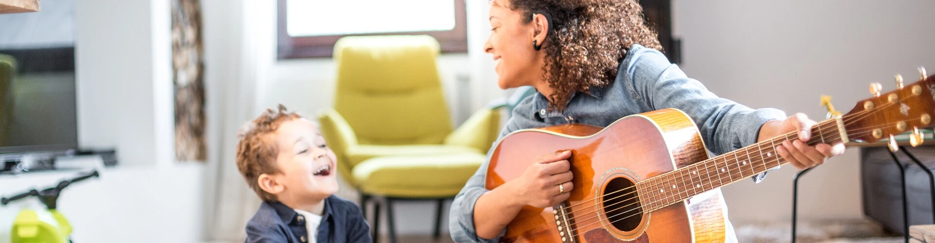 Person playing a guitar, wearing a SONNET 2 EAS audio processor, interacting with a child nearby.