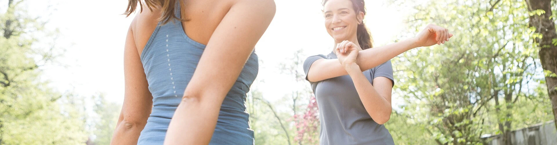 Two people stretching outdoors; one person wears a SONNET 2 EAS audio processor behind the ear.