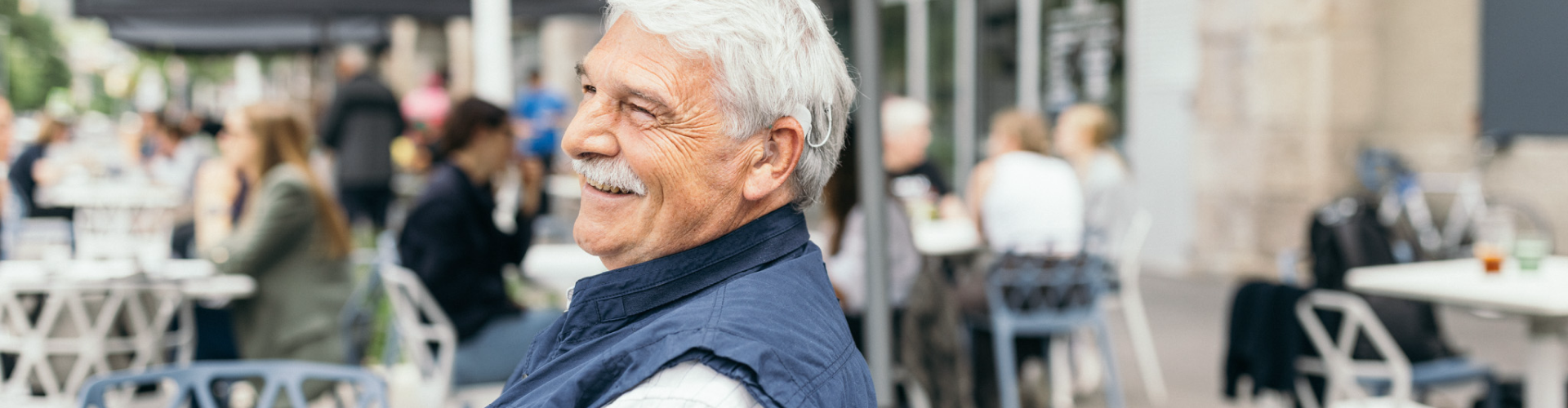 elderly man smiling while using SONNET 3 at a noisy café