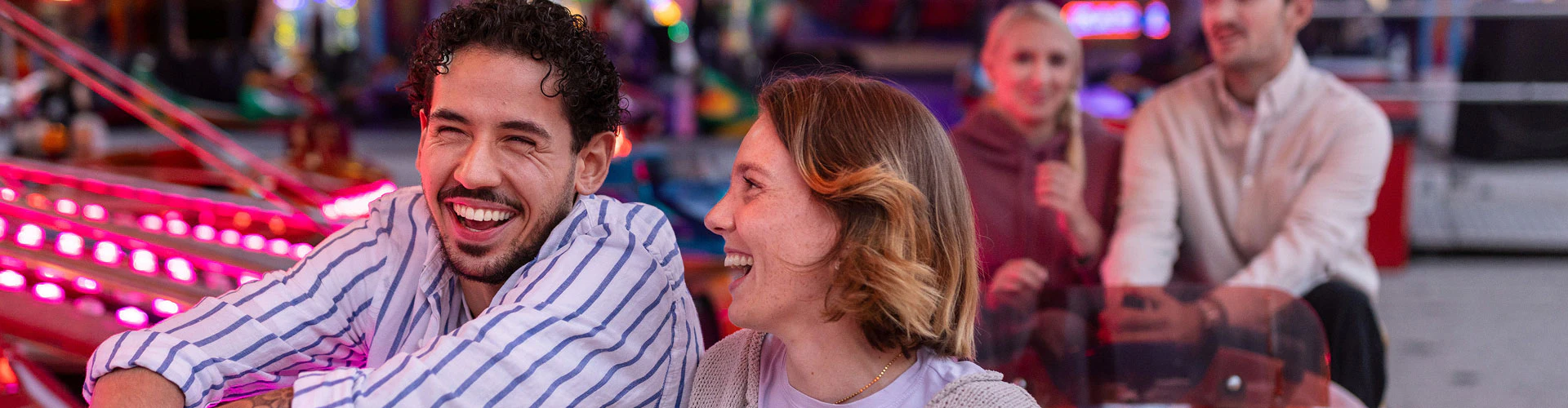 Two people enjoying a fairground ride with colorful lights in the background.